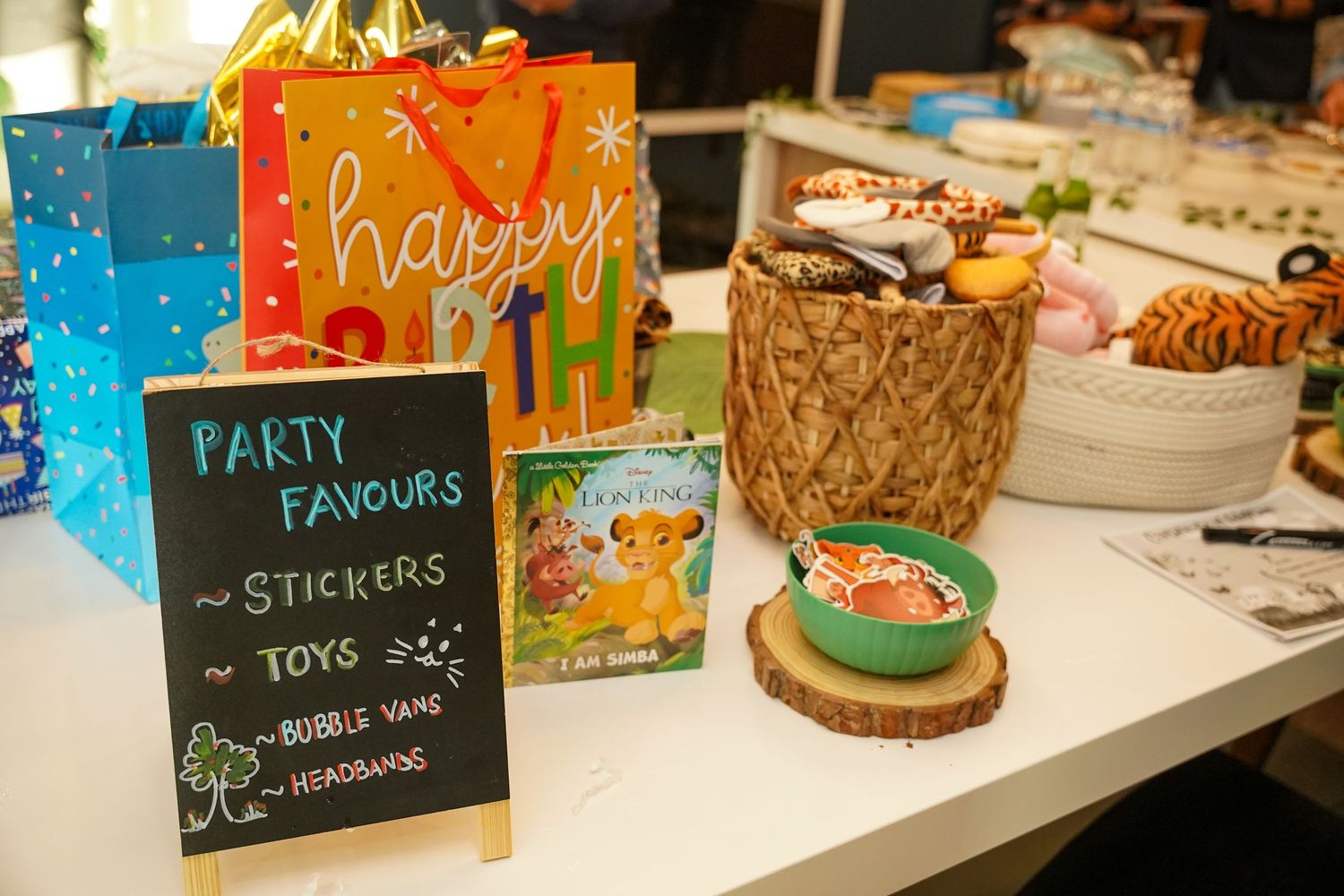 Party favors display table with colorful gift bags and chalkboard sign listing items.