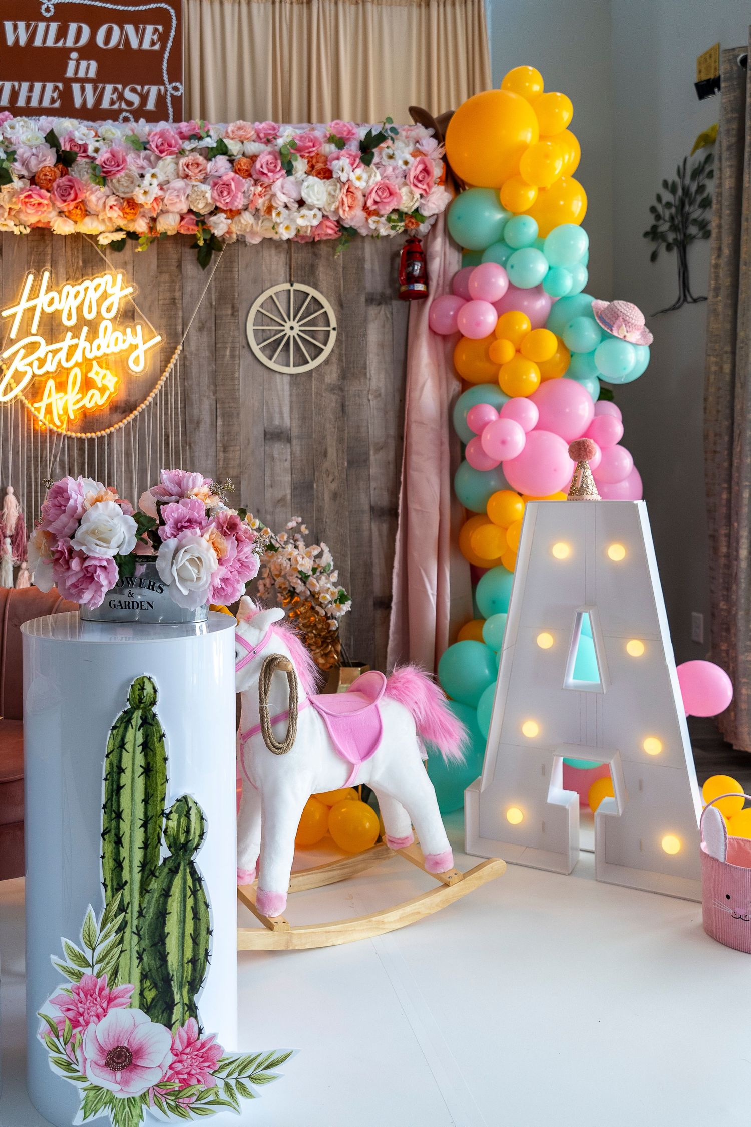 Western-themed party decoration with balloon arch, floral garland, and illuminated letter A.