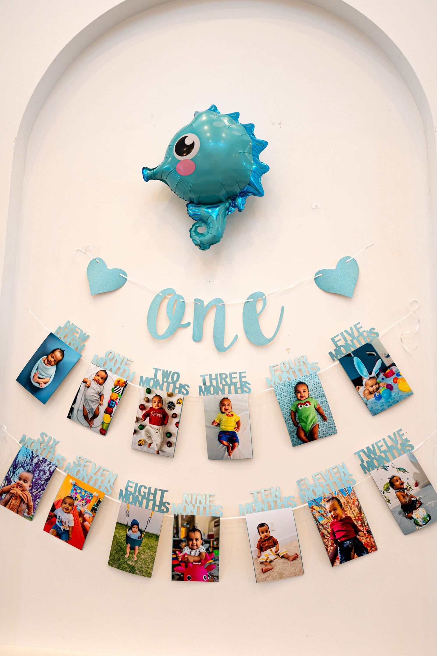 First birthday photo display with blue pufferfish balloon and milestone pictures on string.