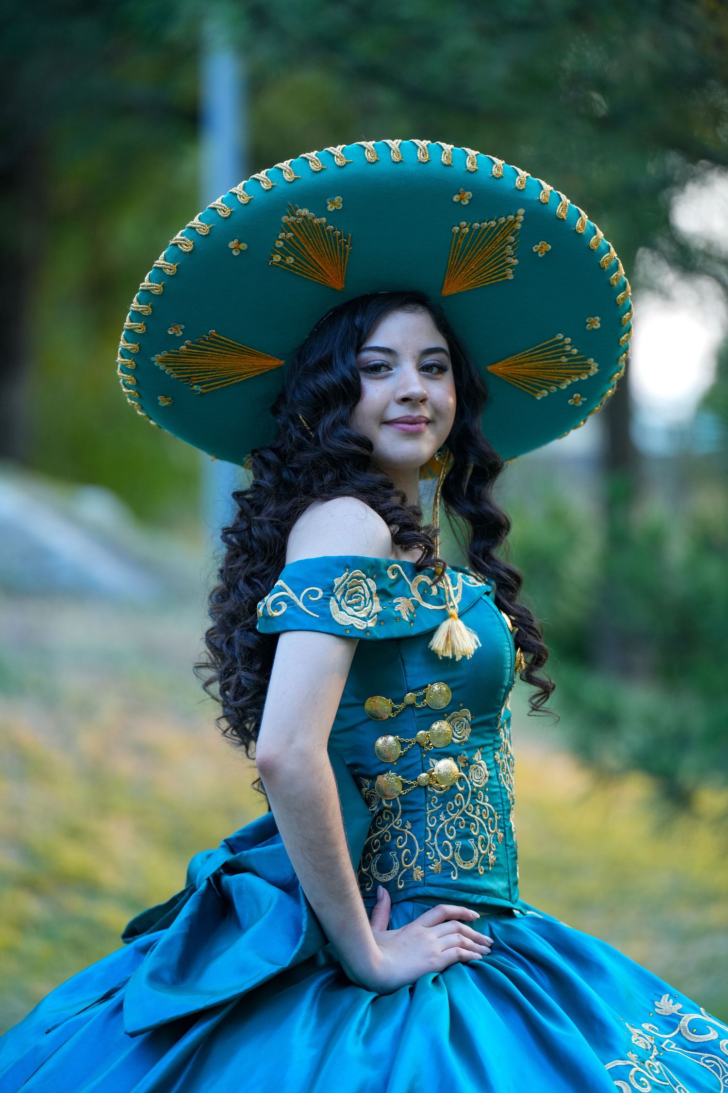 Traditional quinceañera dress in turquoise with ornate sombrero and gold embellishments.