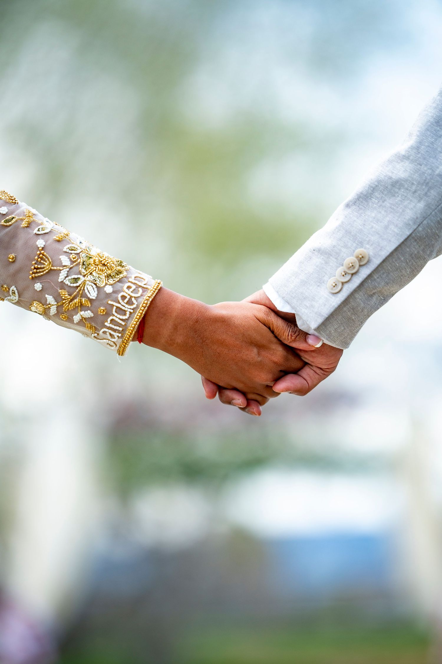 Close-up of couple holding hands showing intricate gold sleeve details.