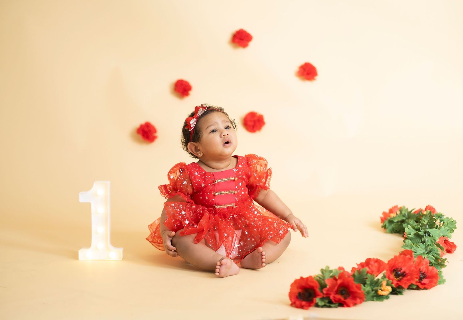 First birthday photoshoot with red floral decorations and white number one on beige background.