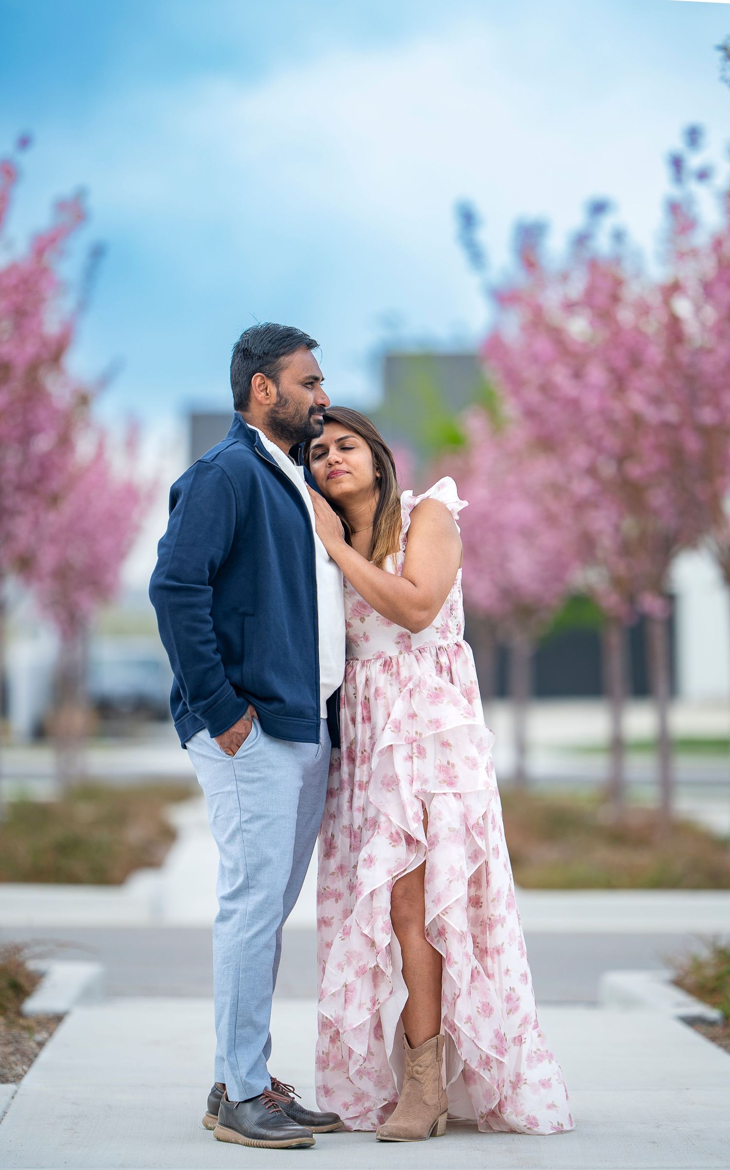 A romantic couple poses together under blooming cherry blossom trees in spring.