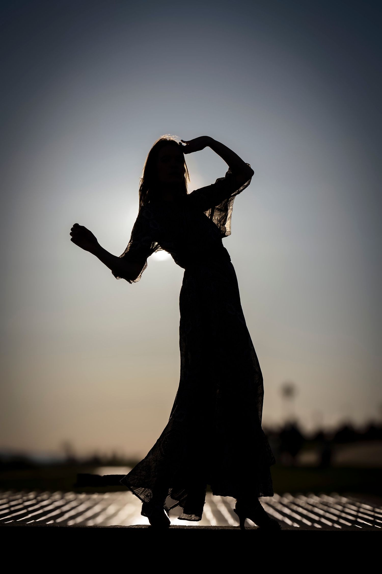 Silhouette of a dancer in flowing dress striking graceful pose against sunset sky.