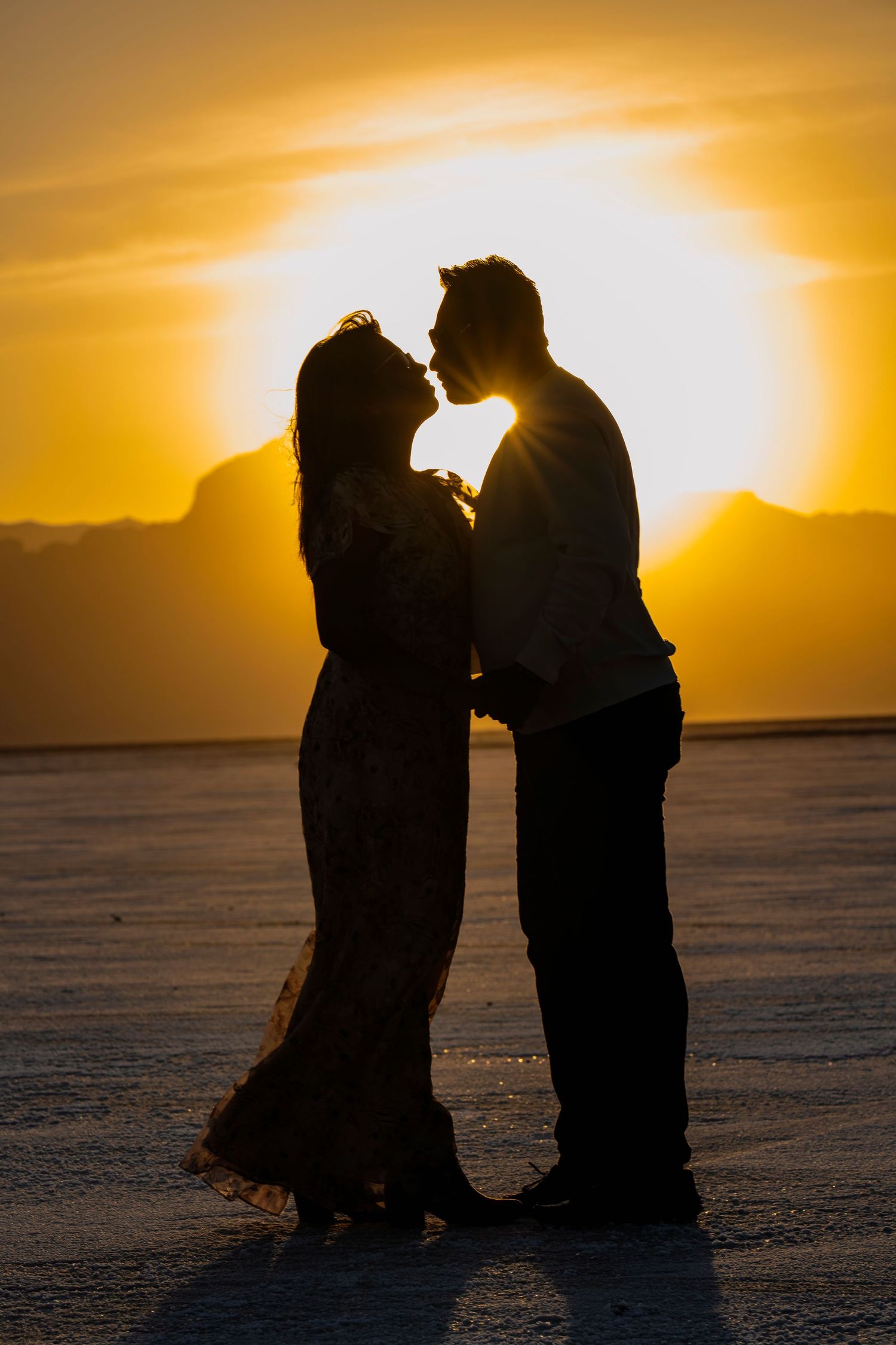 A romantic silhouette of a couple against a golden sunset in a desert landscape.