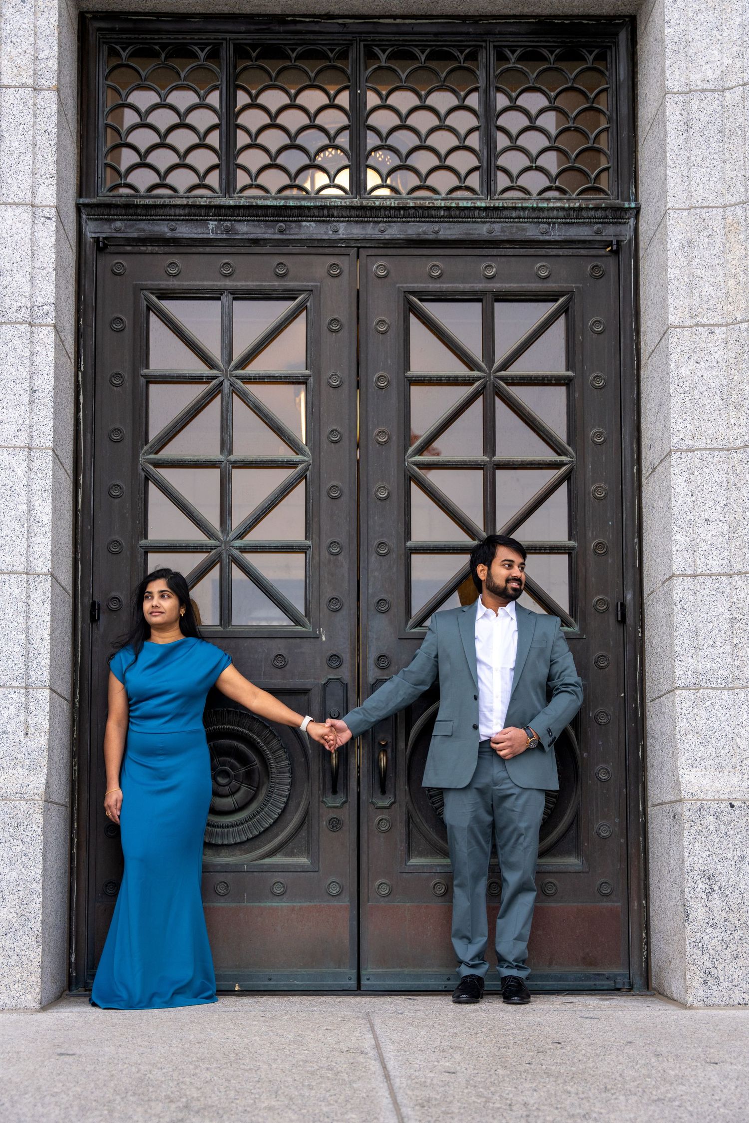 Stylish couple in formal attire posed against ornate metal door.