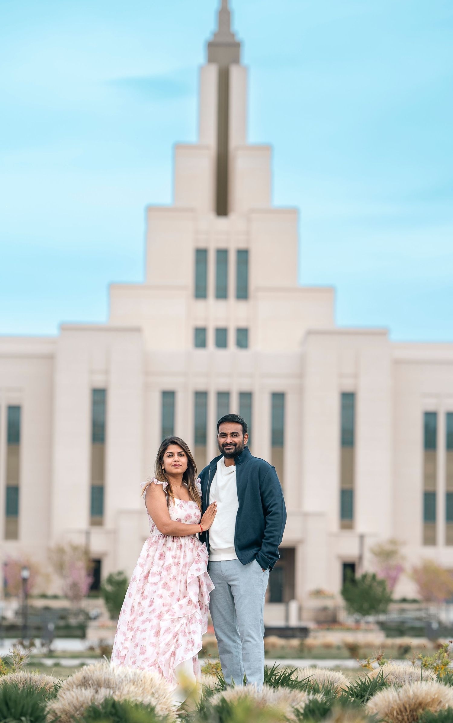 A couple shares a romantic moment in front of an elegant white temple building.