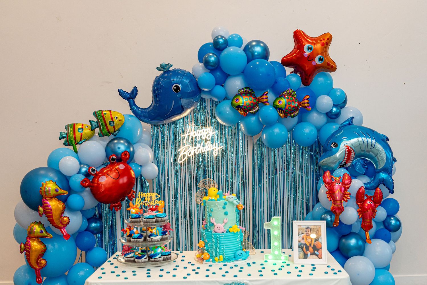 Under the sea themed party backdrop with blue balloon arch and marine creature decorations.