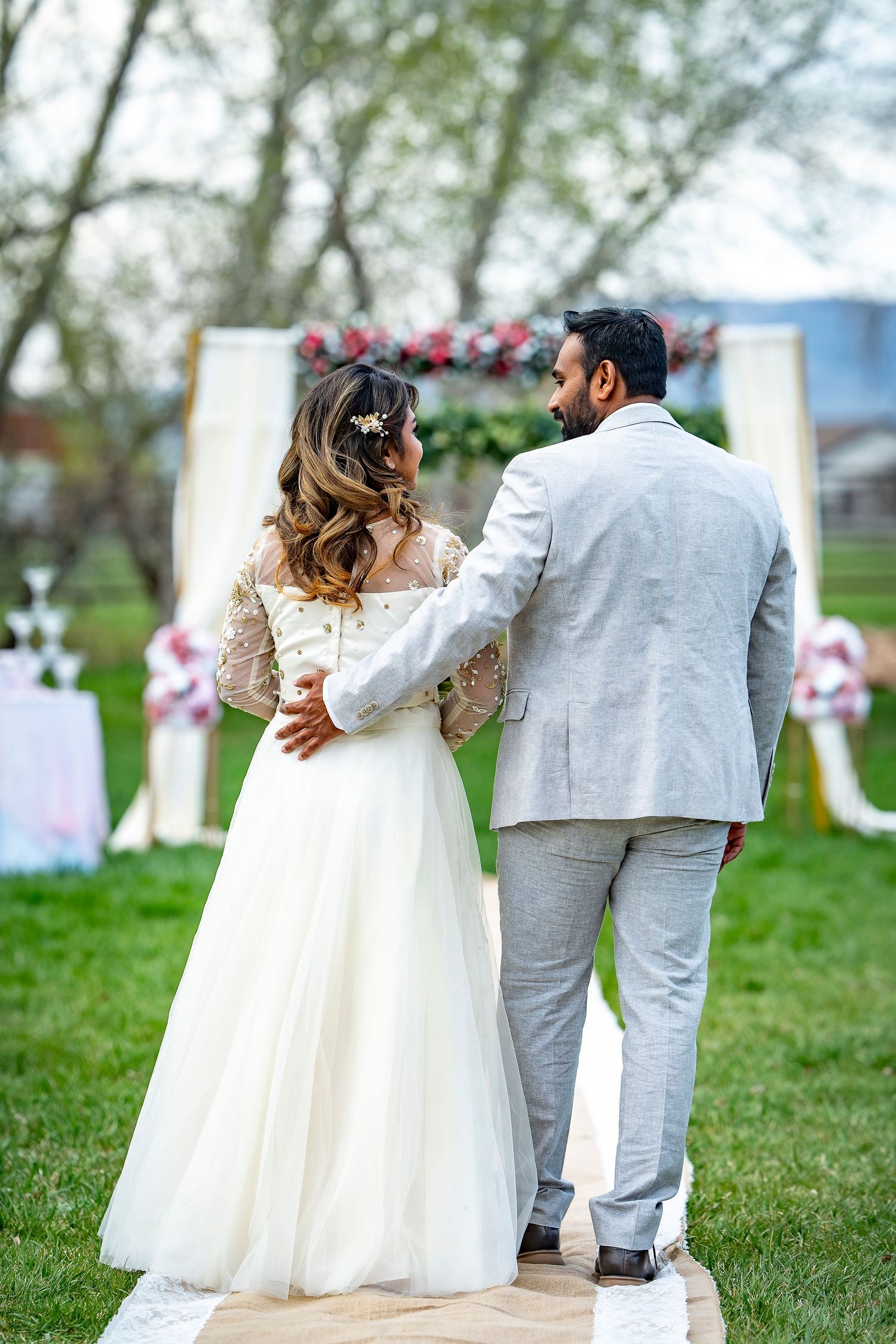 Back view of couple standing on white aisle runner with floral arch.
