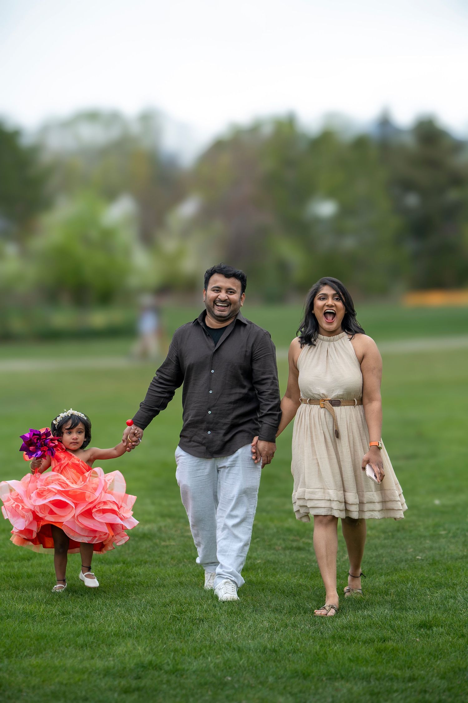 A family walks together on green grass with a child wearing a fluffy coral dress.