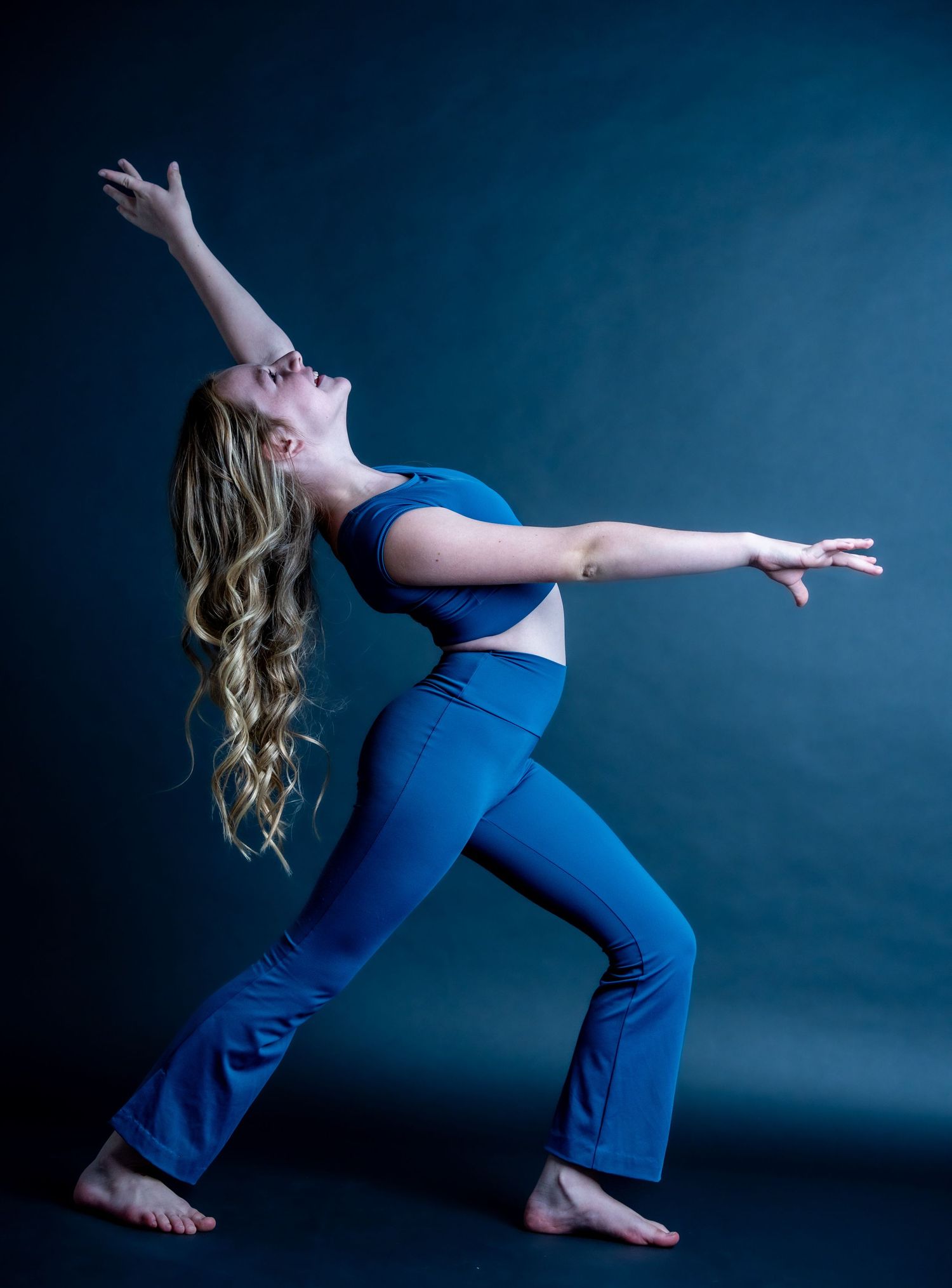 Athletic dancer in blue workout attire strikes a dramatic pose against dark background during dance performance.
