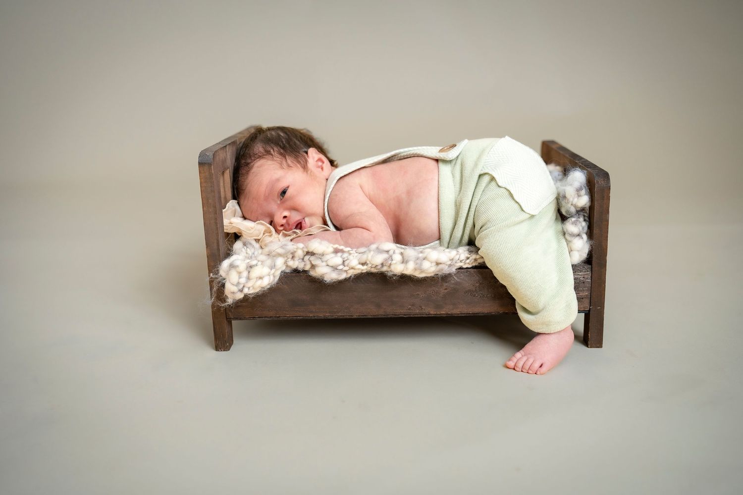 Infant resting on wooden bed with soft blanket in studio setting.