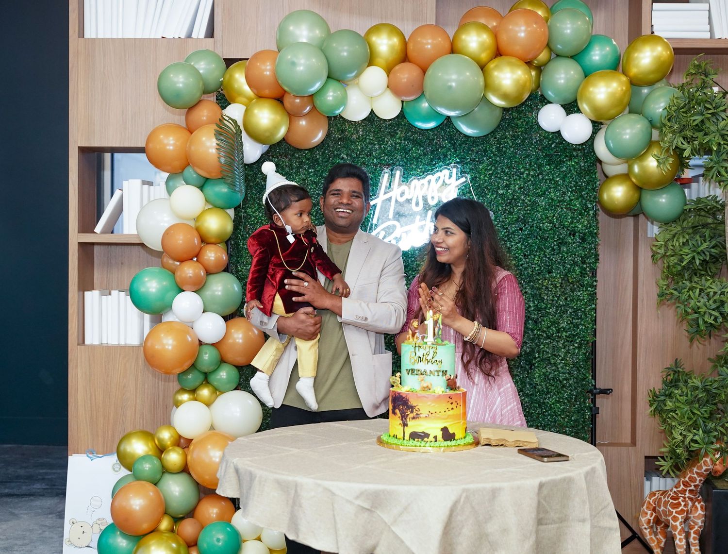 Festive birthday party setup with gold and green balloon arch over a white table with cake.