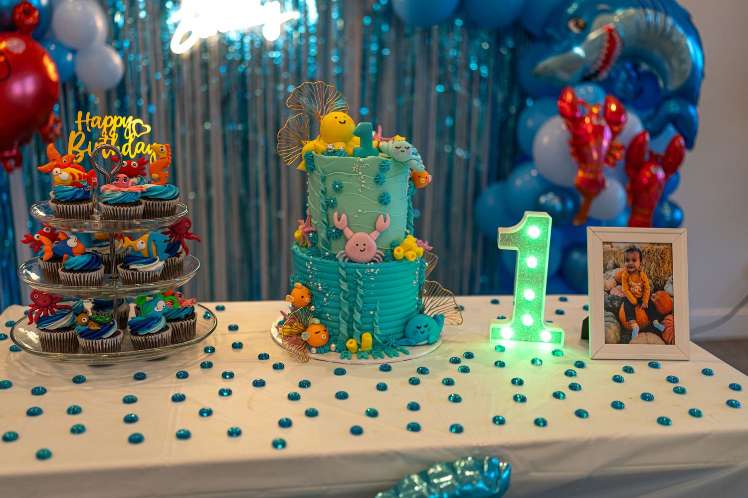 Ocean-themed first birthday party table with teal cake and decorations.