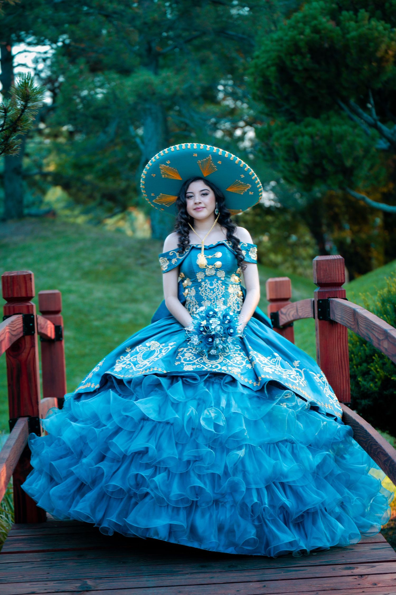 Stunning turquoise quinceañera gown with ruffled skirt photographed on wooden bridge.