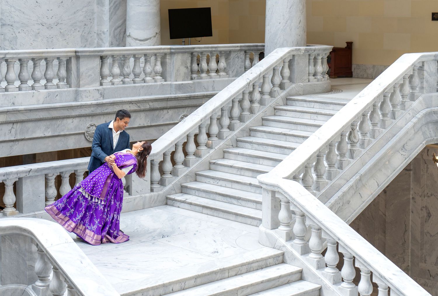 Couple seated on elegant white marble staircase with ornate balustrades.