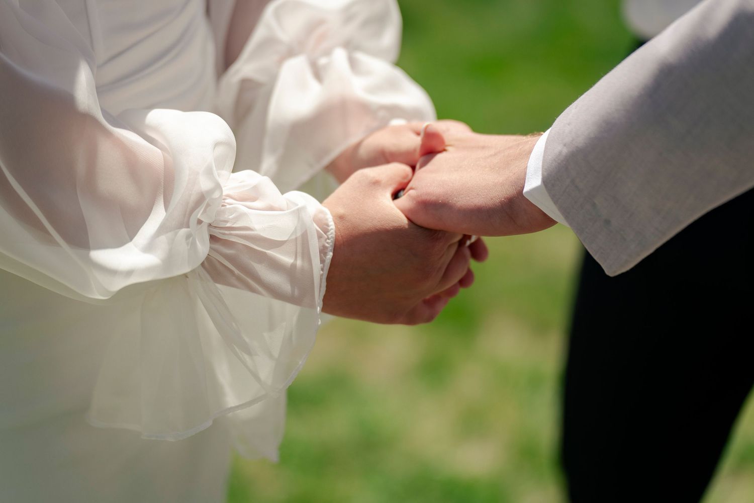 Close-up shots of hands exchanging rings during an outdoor wedding ceremony.