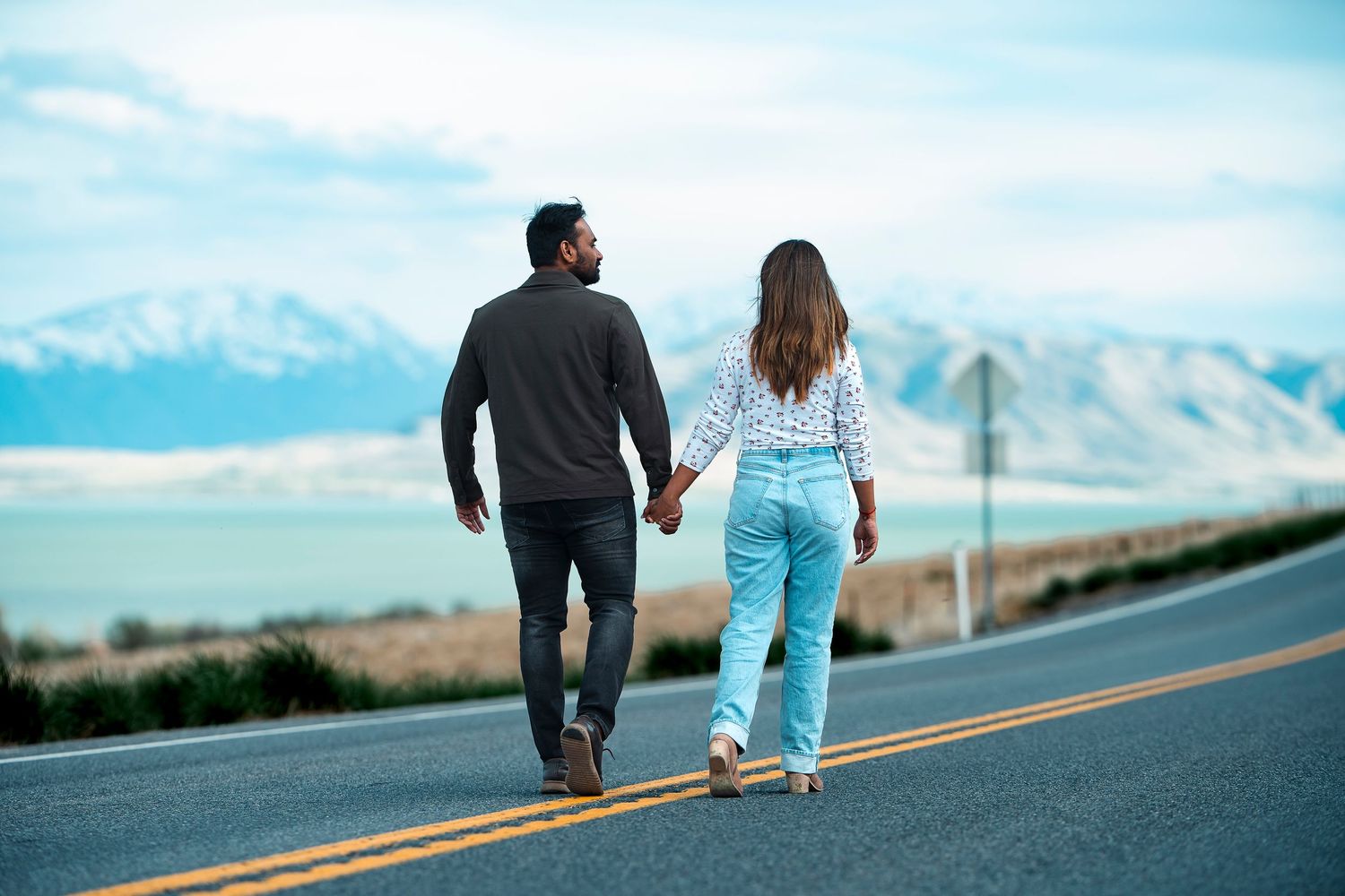 A couple walks hand in hand along a scenic mountain road with dramatic views.