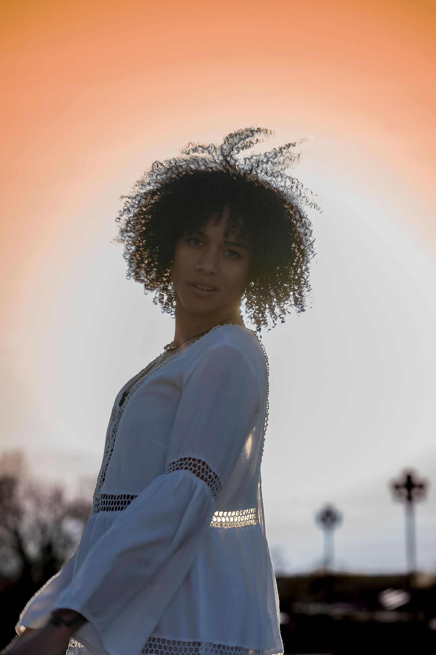 Stylish portrait of person in white dress with natural curly hair against sunset sky.