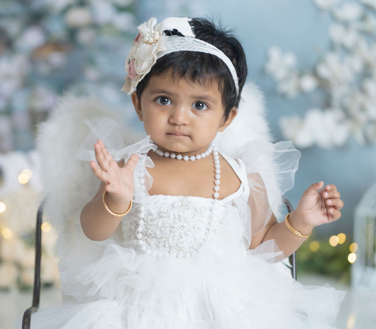 A white tulle dress with pearls and headband against a blue bokeh background.