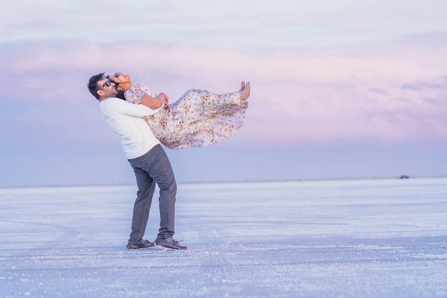 A couple plays and dances together on a beach at sunset.