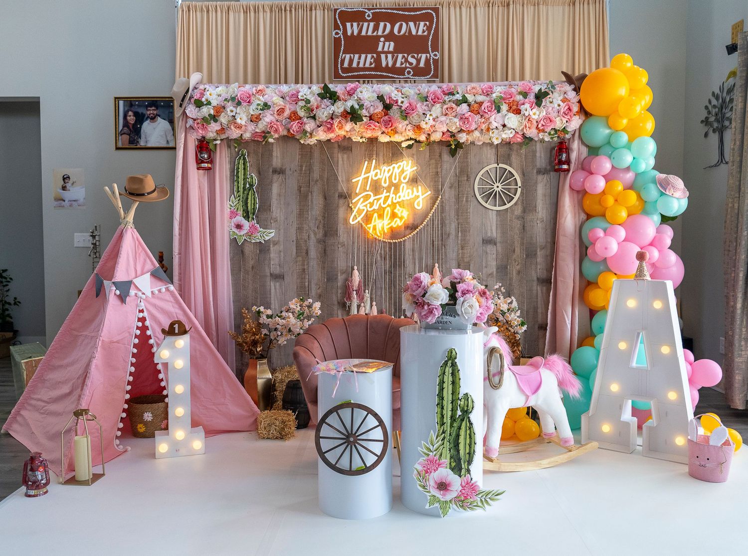 Wild West themed party setup with pink teepee, balloon arch, and rustic backdrop.