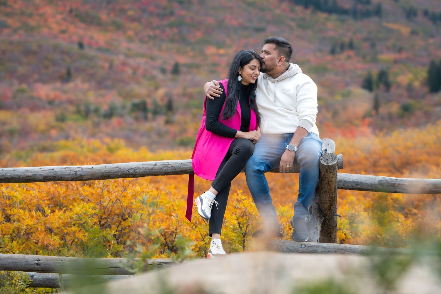 Couple sharing romantic moment on fence overlooking autumn mountain landscape.