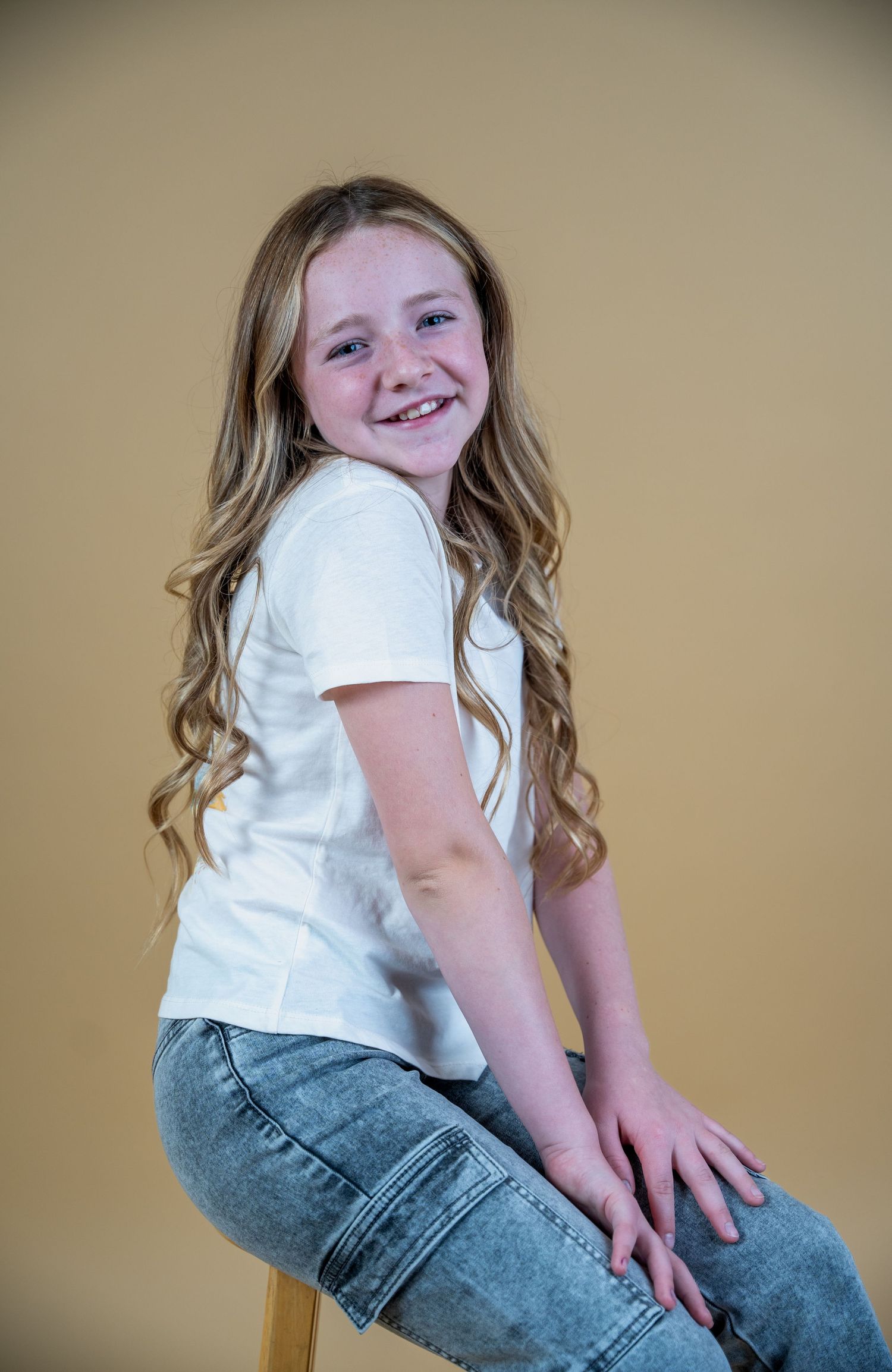 Portrait of person in white t-shirt and jeans sitting on stool.