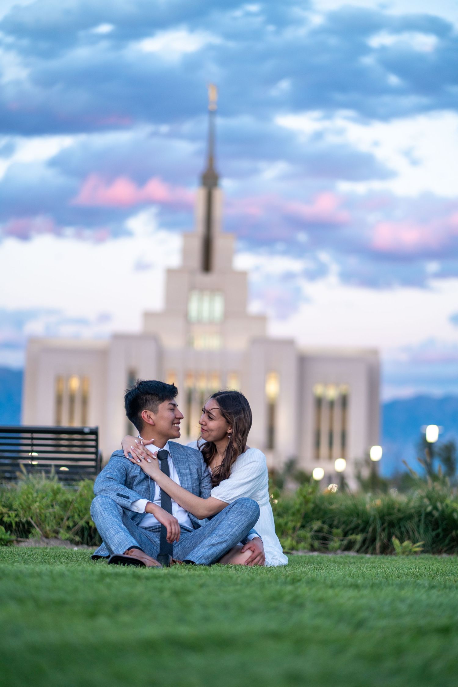 Couple sitting on grass in front of Mormon temple during blue hour.