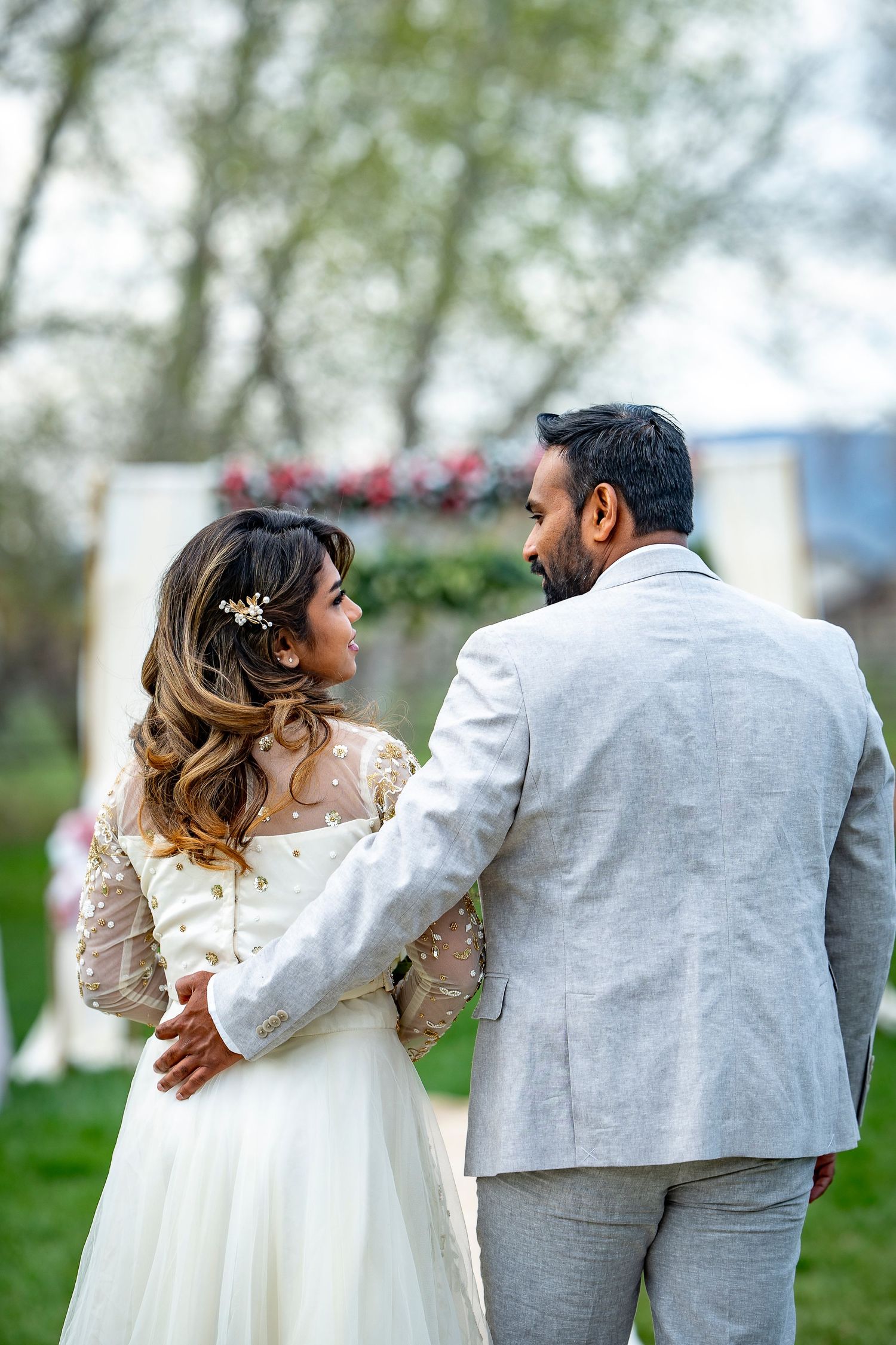 Wedding couple in lace and gray suit photographed from behind in a spring garden setting.