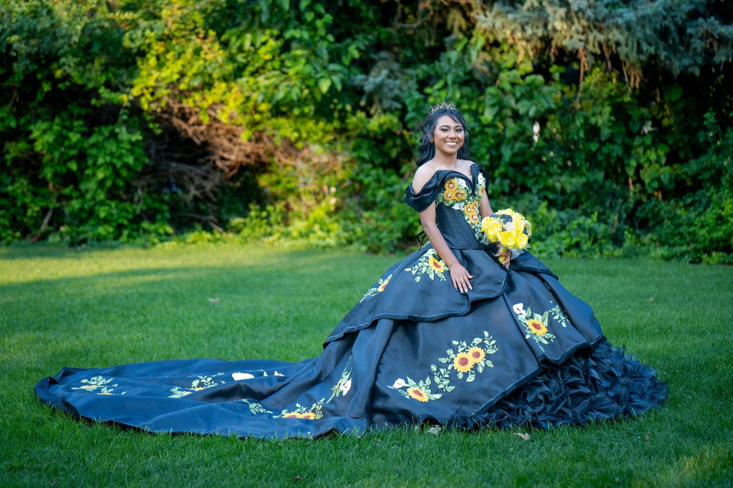 Person in dramatic black and yellow floral ballgown poses in garden setting.