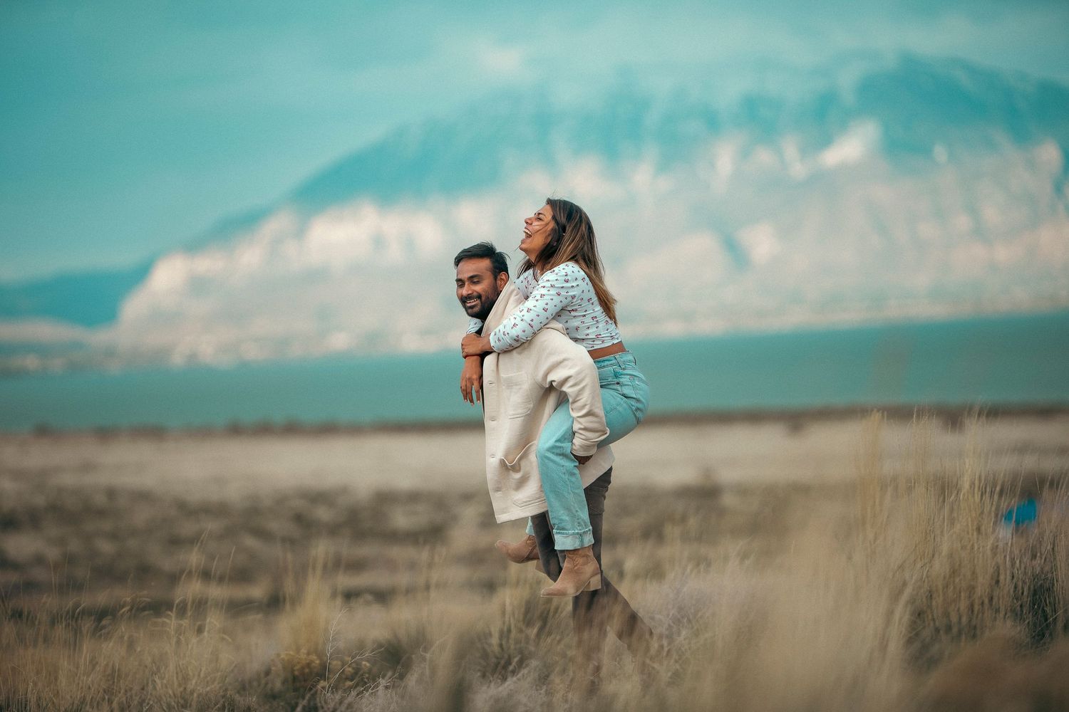 A couple embraces in a field with mountains and dramatic sky in the background.