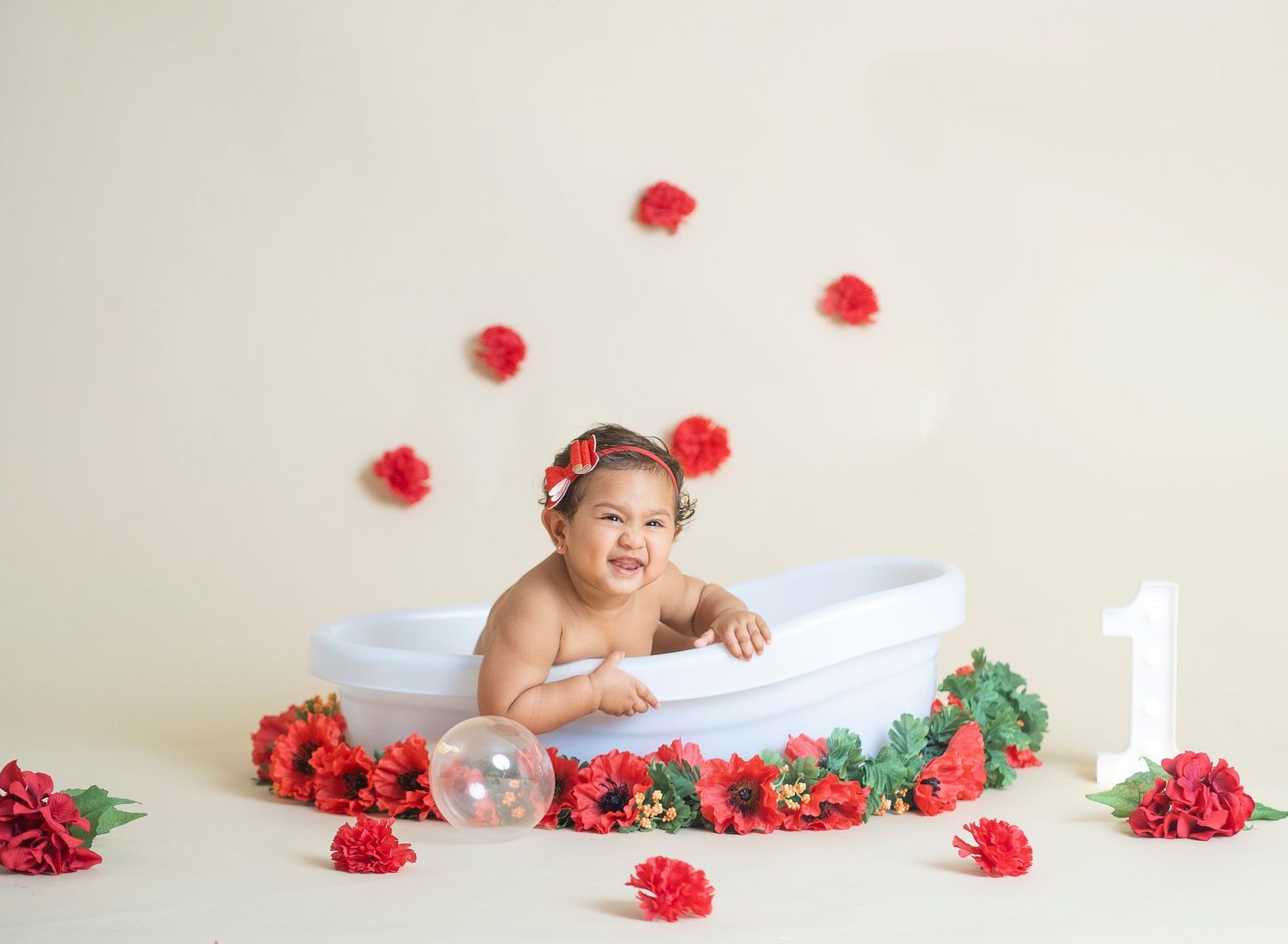 First birthday portrait session with red roses and white bathtub prop on neutral background.