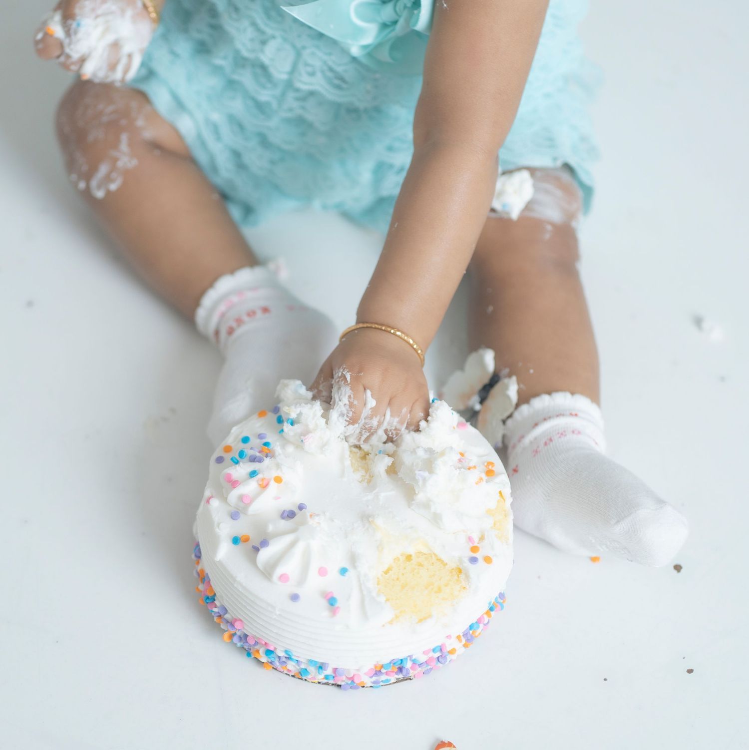 Small hands smashing into a white birthday cake with colorful sprinkles.