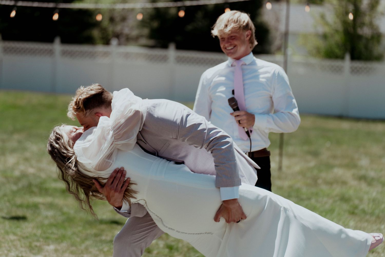 A playful dip dance move at an outdoor wedding celebration in sunlight.