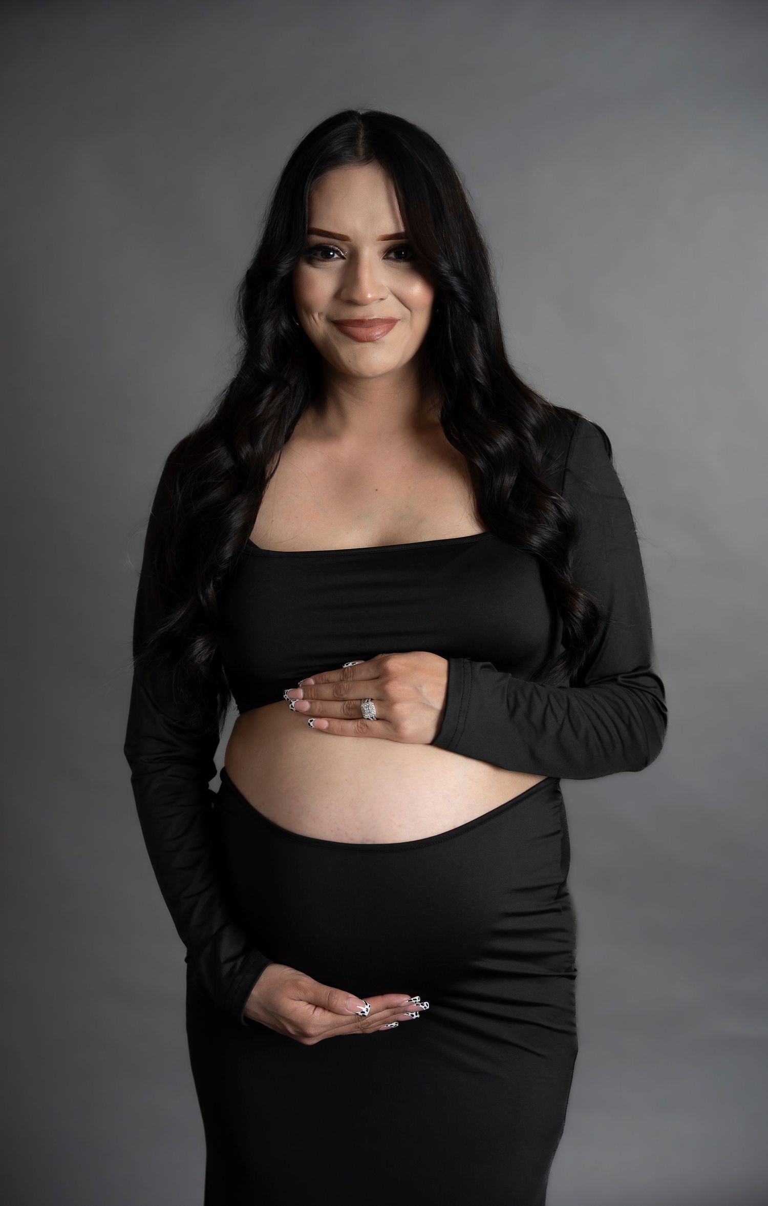 Elegant maternity portrait in black outfit against grey studio background.
