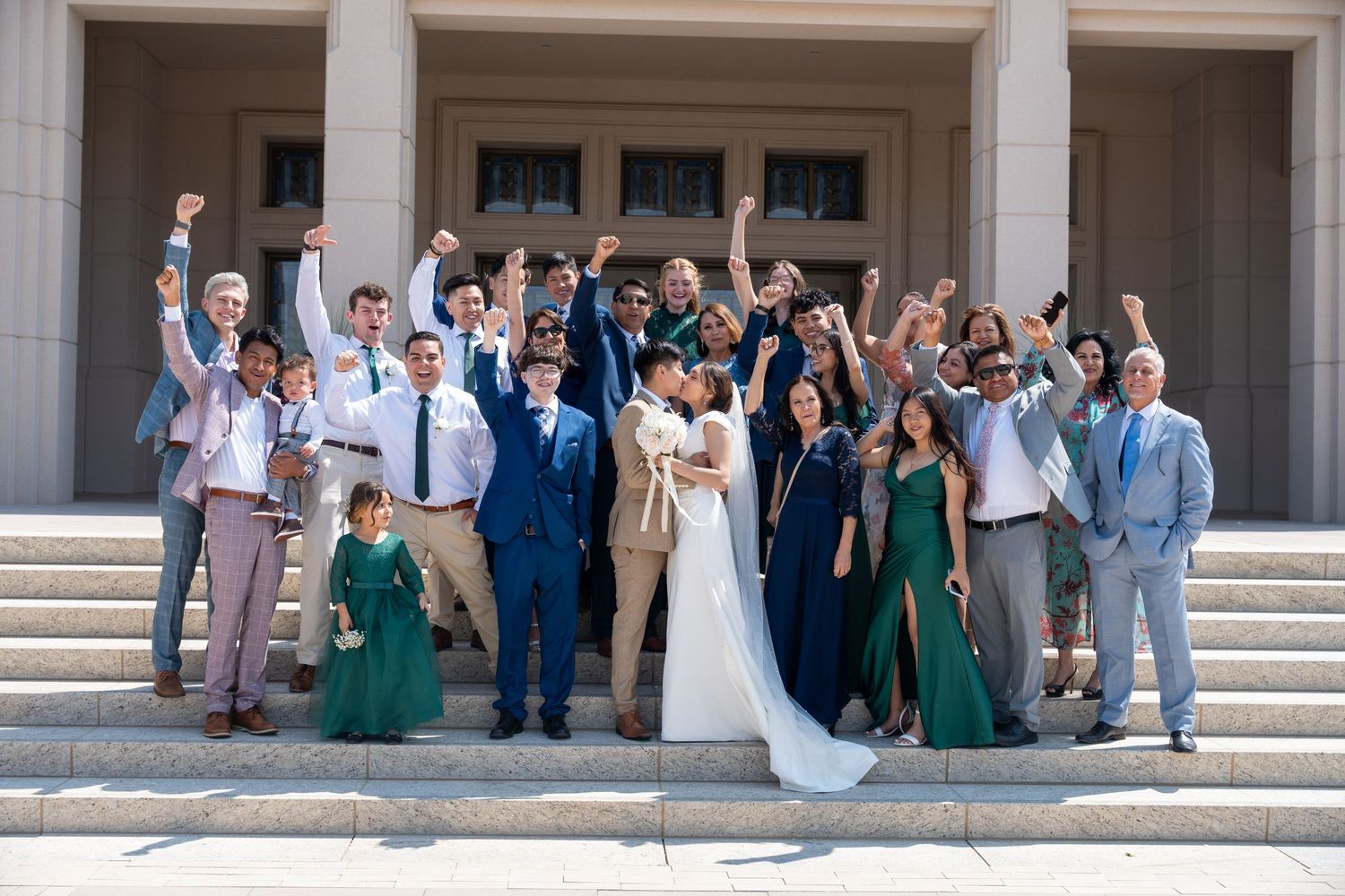 Wedding party celebrating on stone steps of building with colorful attire.