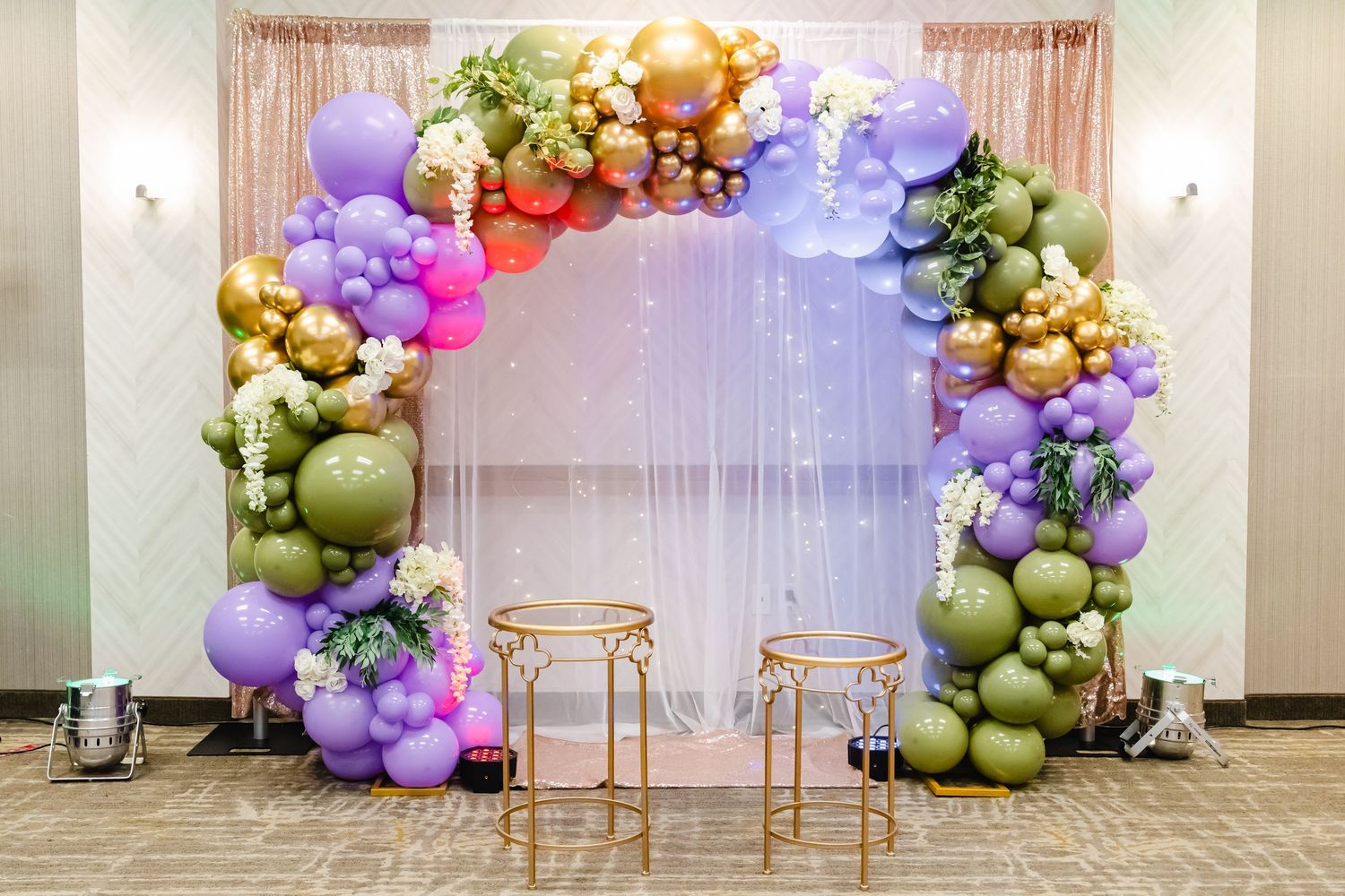 Elegant balloon arch installation with purple and gold balloons framing two gold chairs.
