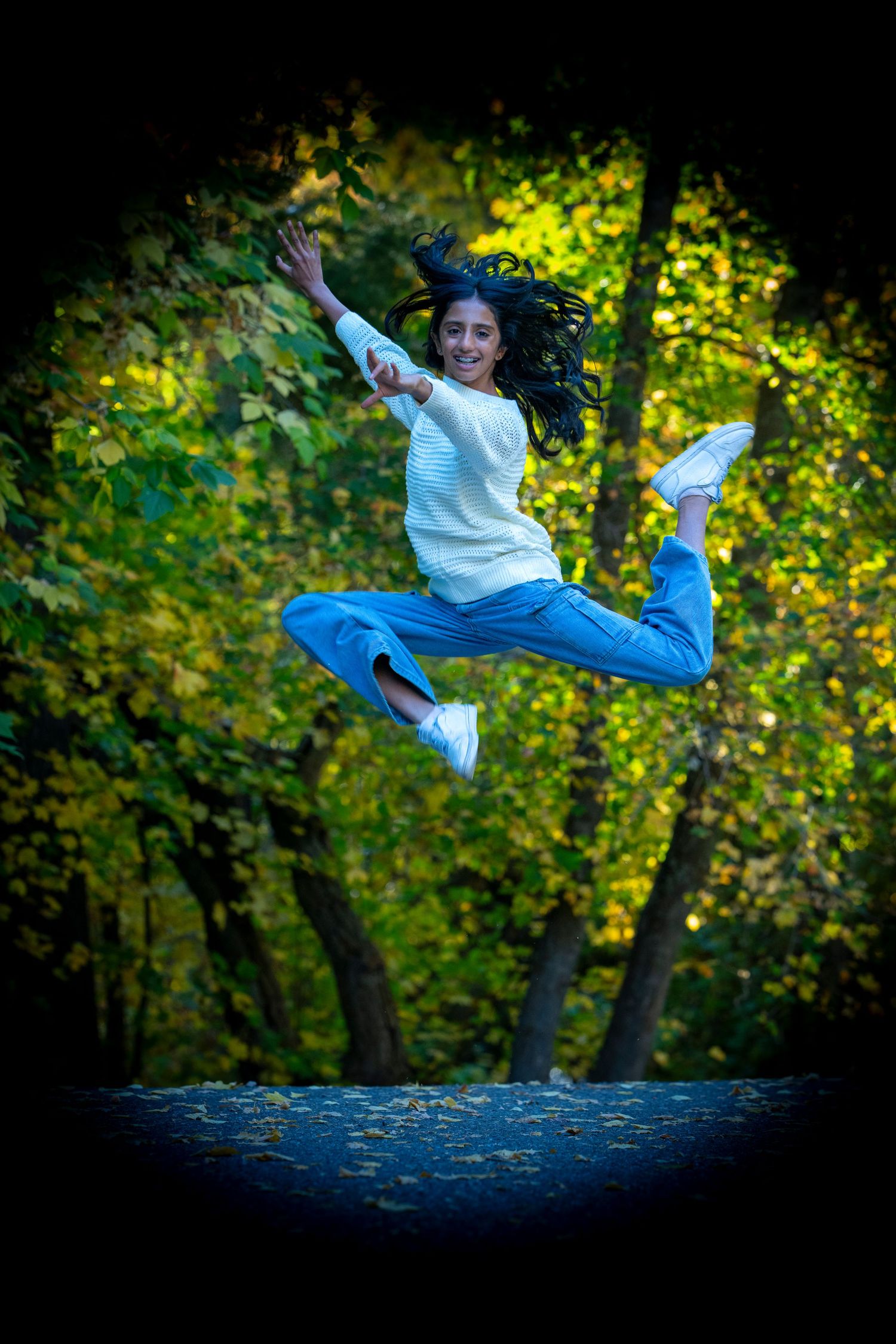Dynamic action shot of person in casual wear performing split jump in wooded setting.