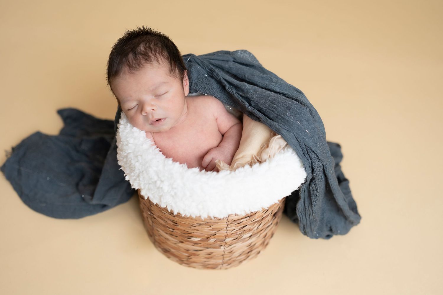 Peaceful newborn portrait in woven basket with soft gray draping.