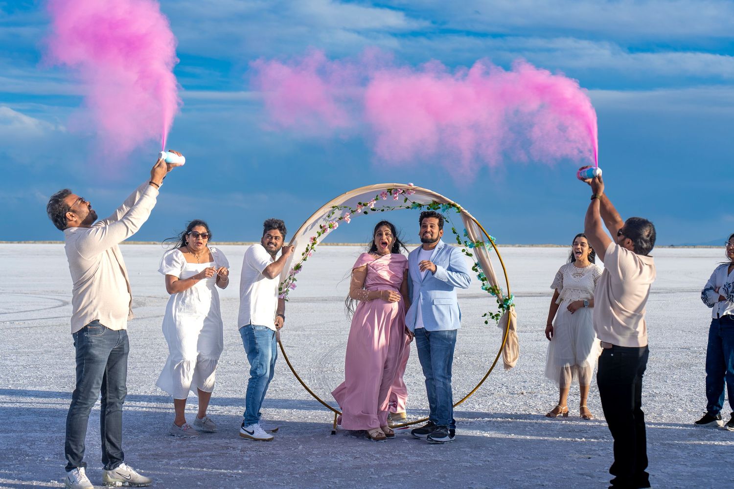 Beach celebration with pink smoke flares and decorative arch on salt flats.