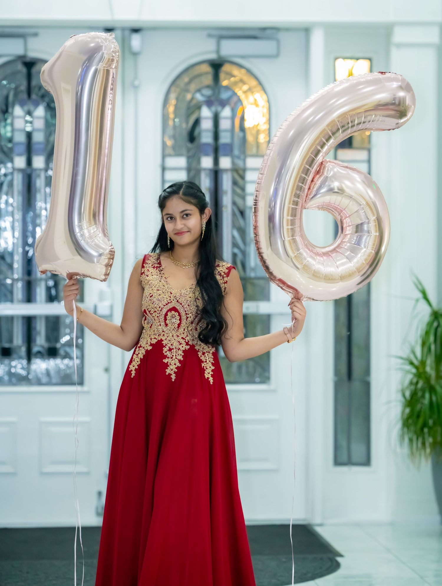 Celebration photo with person in red gown holding silver number 16 balloons.