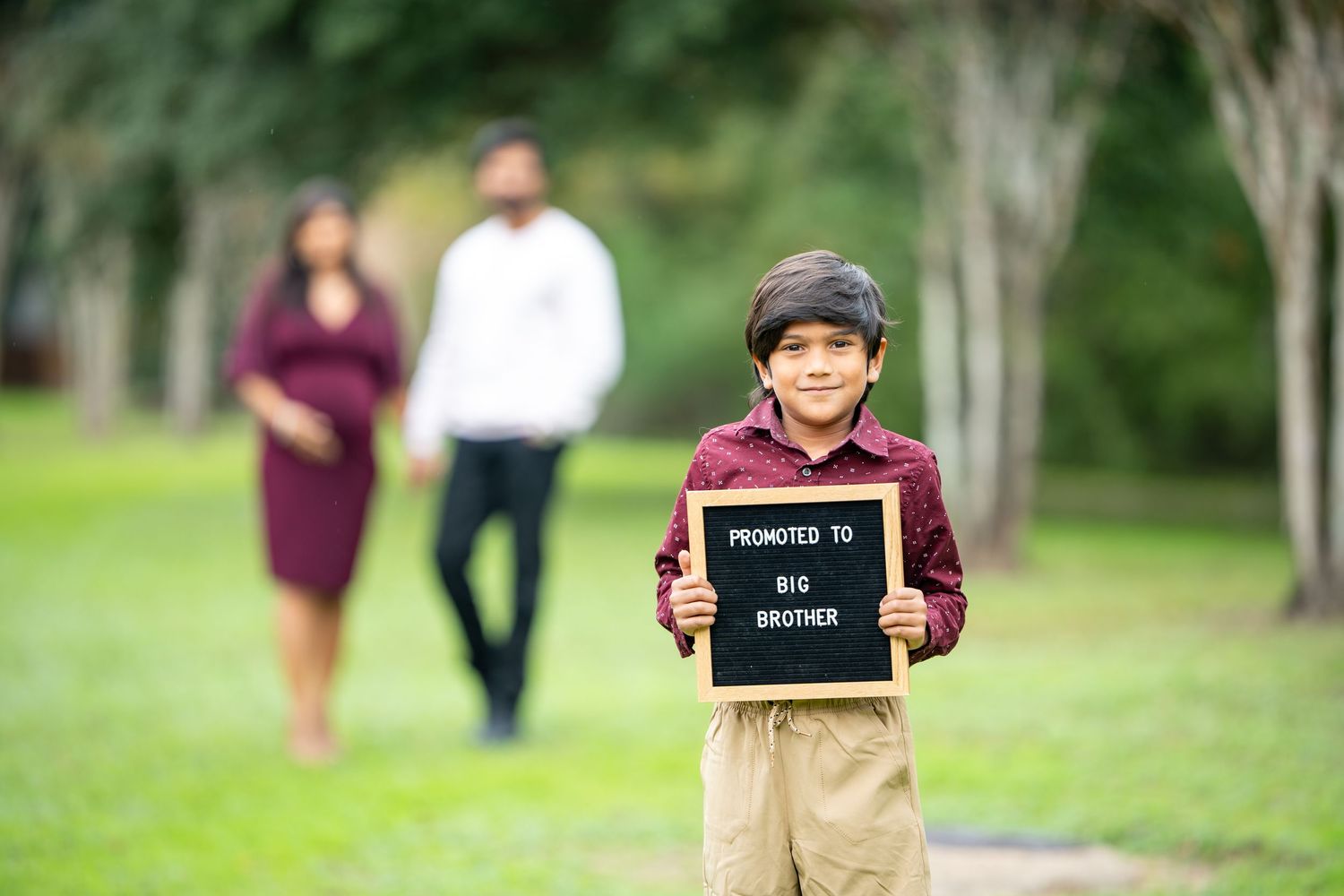 A young boy holds a chalkboard sign while two adults stand in the background.