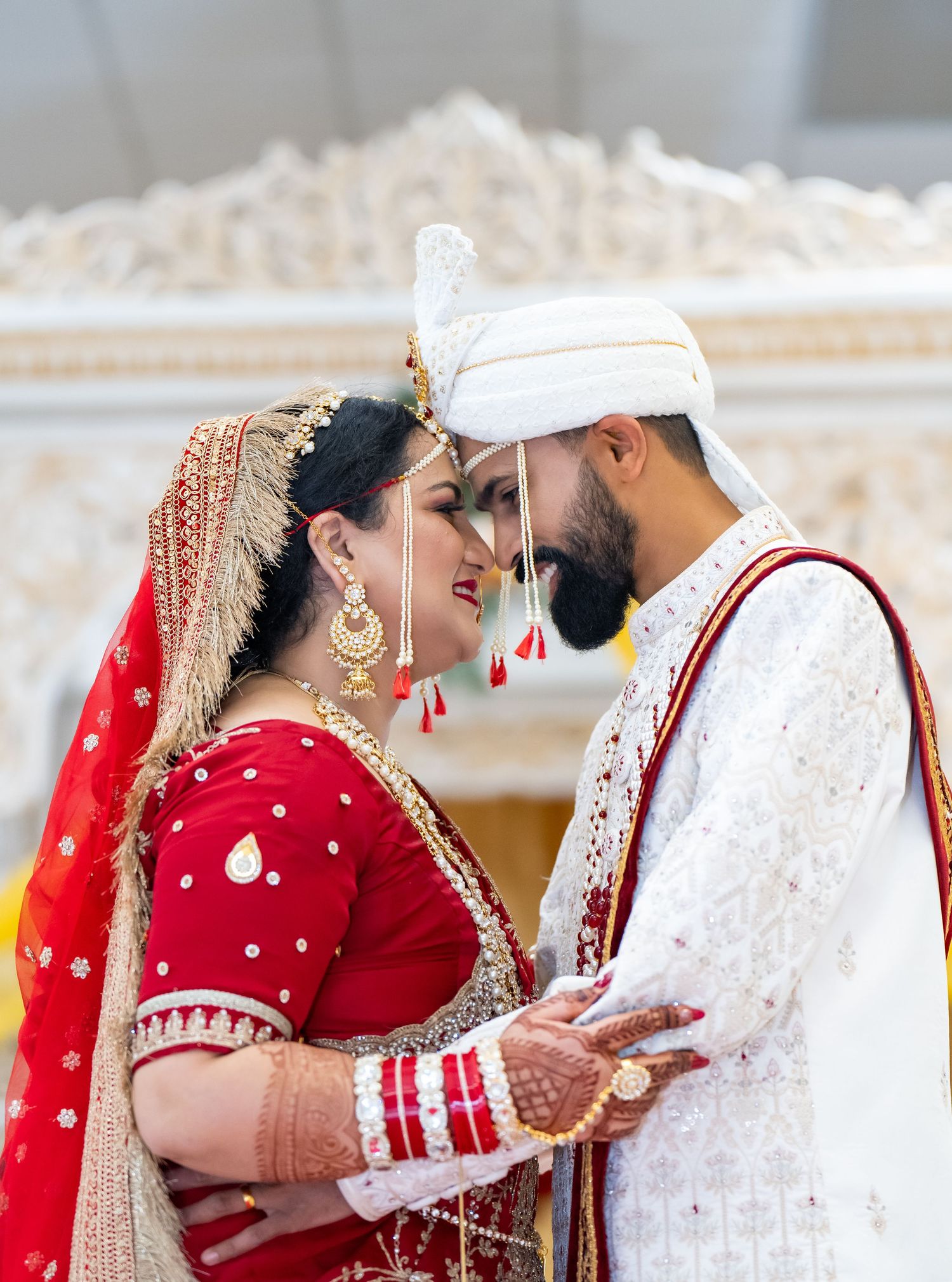 Indian bride in red lehenga and groom in white sherwani share an intimate moment at their traditional wedding ceremony.