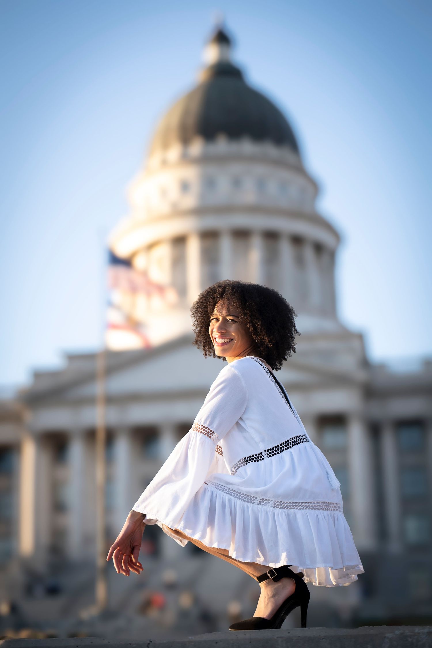 A flowing white dress twirls in front of a domed government building on a sunny day.