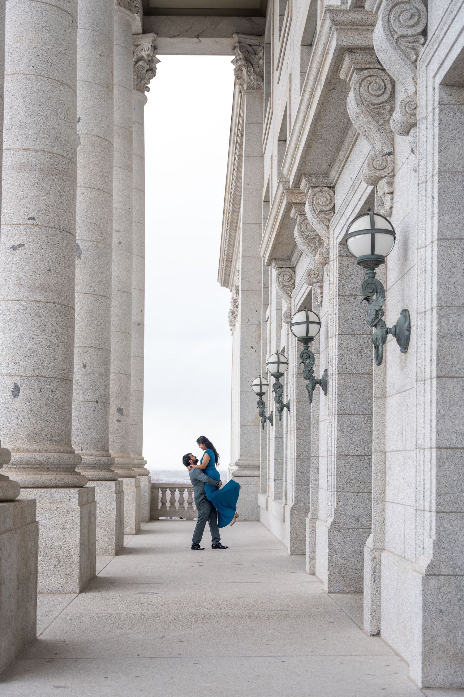 Couple embracing in elegant colonnade with classical architecture.