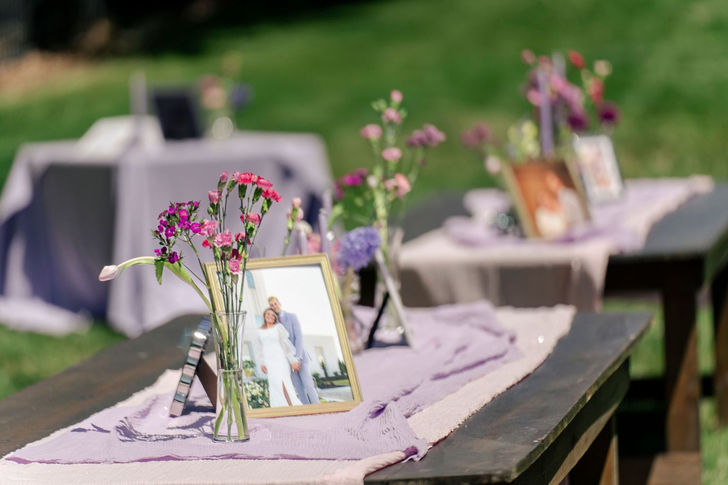 Wedding reception table with purple flowers in vases and framed photos.