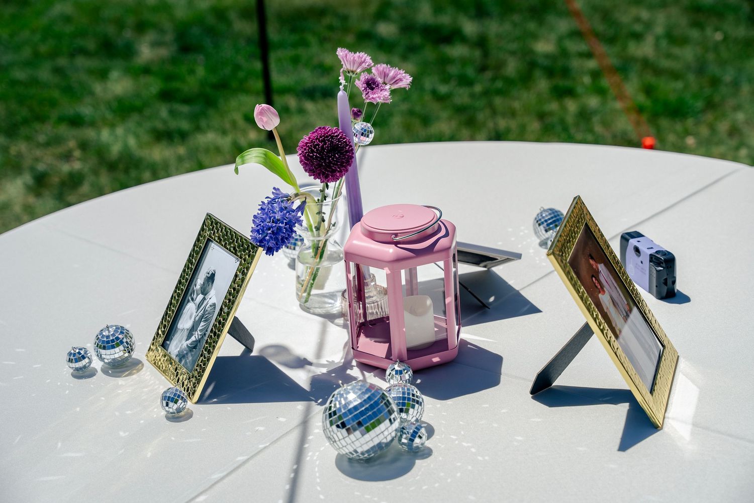 Wedding decor with picture frames, pink jar, and purple flowers on a white table.