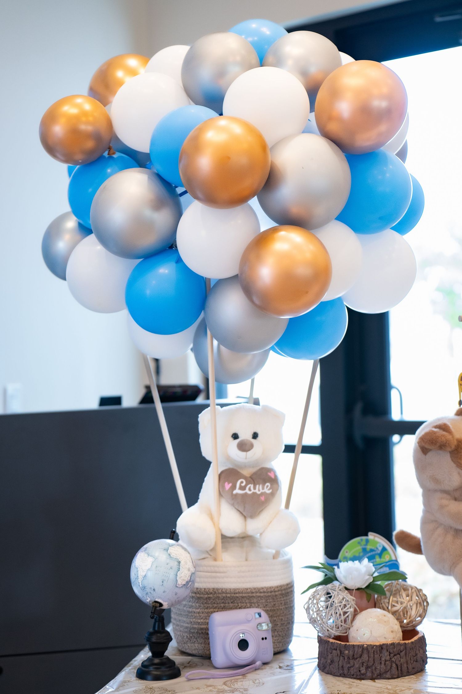 White teddy bear with 'Love' text surrounded by blue, white, and gold balloons.