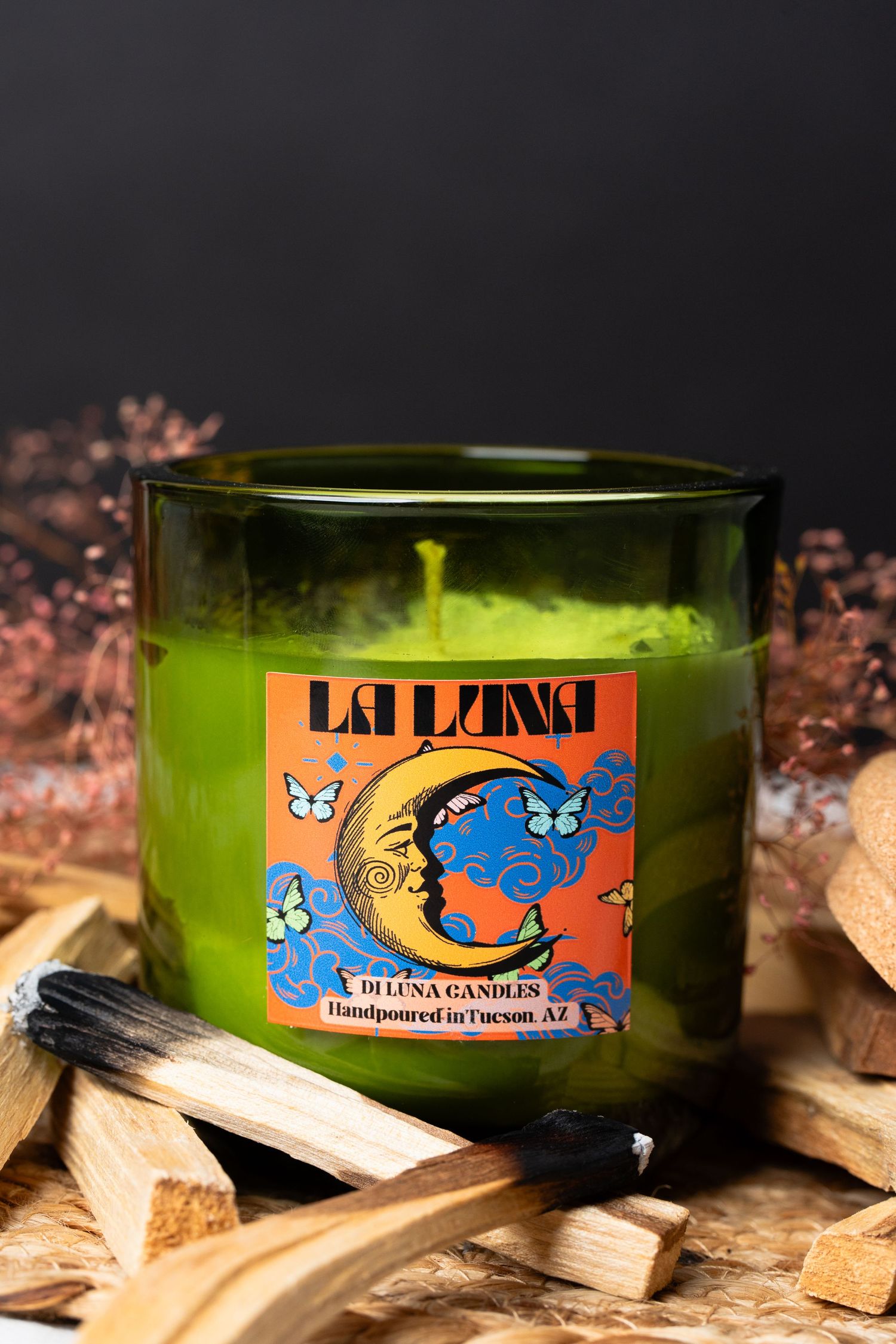La Luna Di Luna green glass candle with vibrant moon goddess label surrounded by wood chips.
